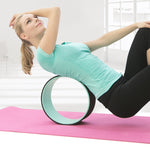 une femme utilise la roue de yoga confort vert d'eau dans son dos sur un tapis d'exercice rose